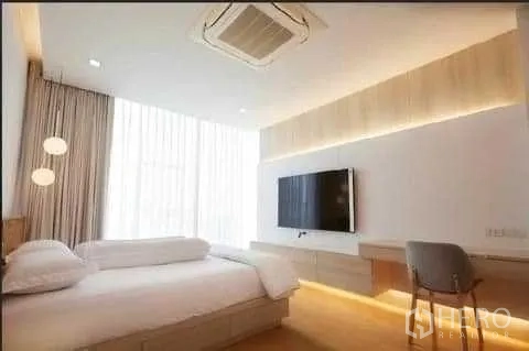 Townhouse for rent in Huai Khwang, Bangkok - Cozy bedroom with wall-mounted TV, work desk, soft lighting and sheer floor-to-ceiling curtains.