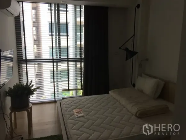 Condominium for rent in Watthana, Bangkok - Cozy bedroom with large window blinds, blackout curtains, wall-mounted TV and a queen bed.