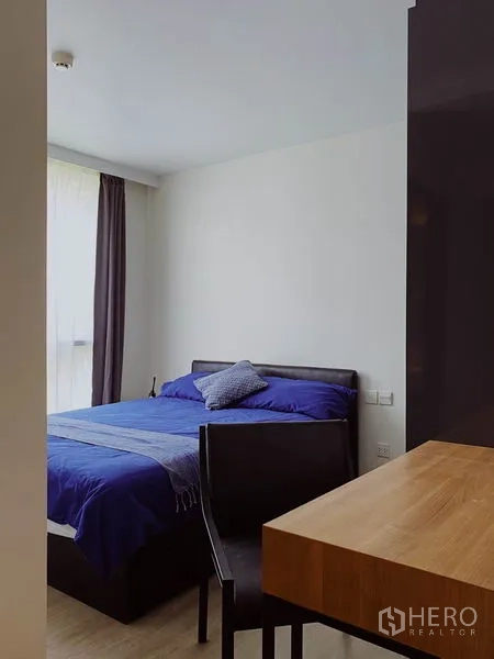 Condominium for rent in Pathum Wan, Bangkok - Master bedroom corner with desk and chair beside a large window and curtains.