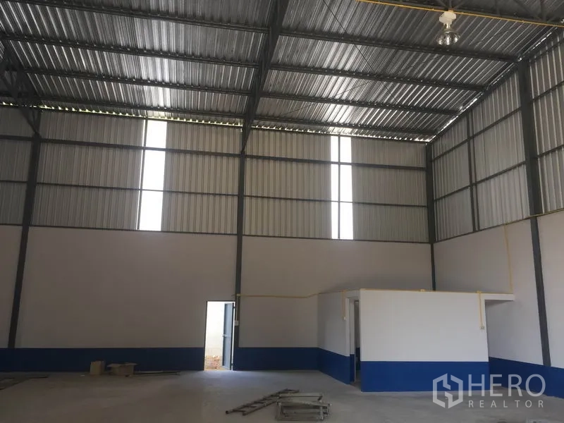 Warehouse for rent in Sai Mai, Bangkok - Tall warehouse interior showing a side entry door and a corner office beneath the high steel roof.