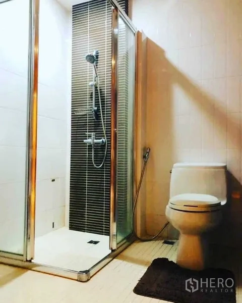 Condominium for rent in Watthana, Bangkok - Modern bathroom with glass-enclosed shower, handheld spray and toilet.