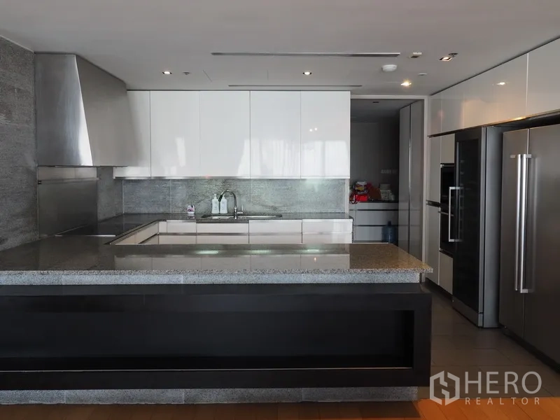 Condominium for rent in Sathon, Bangkok - Modern U-shaped kitchen with stone island, stainless appliances and glossy white cabinets.