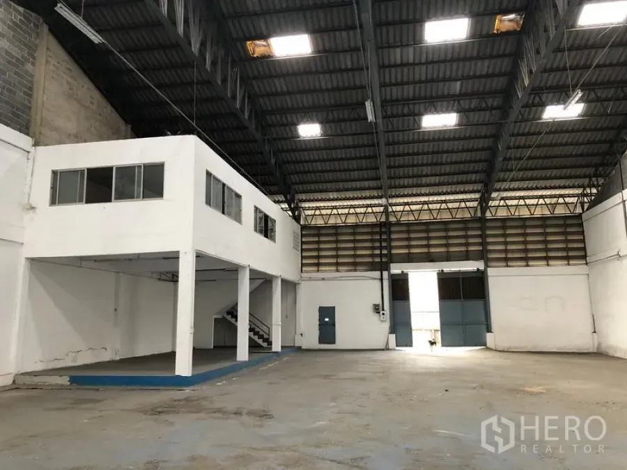 Warehouse for rent in Bang Phli, Samut Prakan - Spacious warehouse interior with high steel truss roof, skylights, and a mezzanine office with stairs.