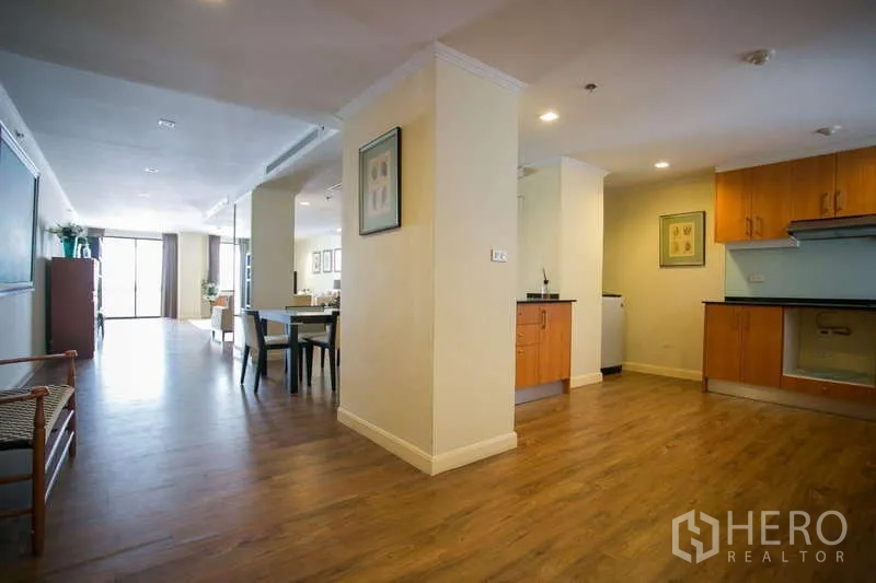 Condominium for rent or sale in Watthana, Bangkok - Open-plan dining area beside U-shaped kitchen with wood cabinetry.