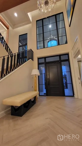 Detached House for rent or sale in Saphan Sung, Bangkok - Double-height foyer with black-framed glass door, chandelier, herringbone floor, and staircase.