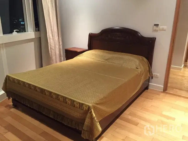 Condominium for rent in Khlong Toei, Bangkok - Cozy bedroom with dark wood bed, gold bedspread, window, and bedside table.