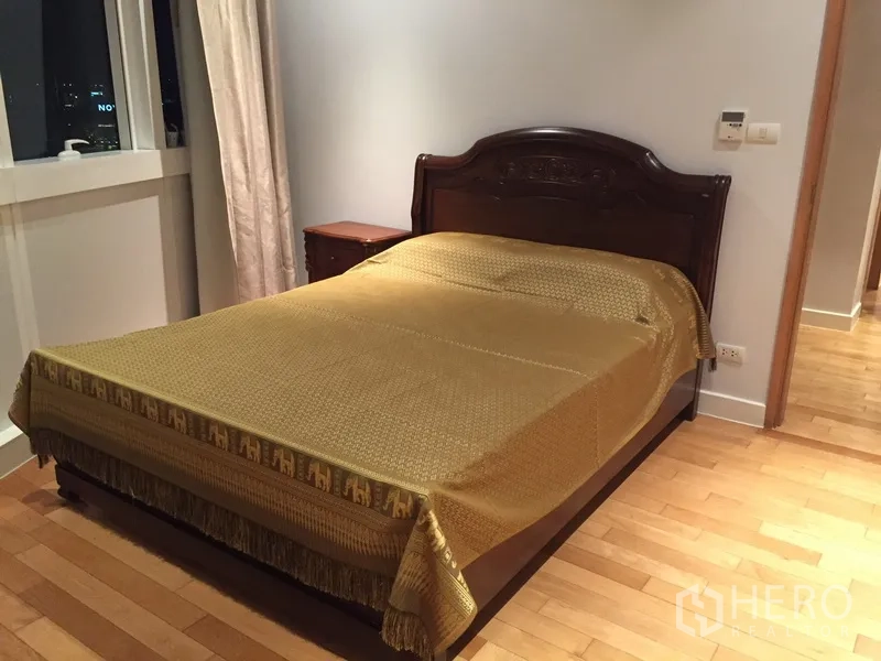 Condominium for rent in Khlong Toei, Bangkok - Cozy bedroom with dark wood bed, gold bedspread, window, and bedside table.