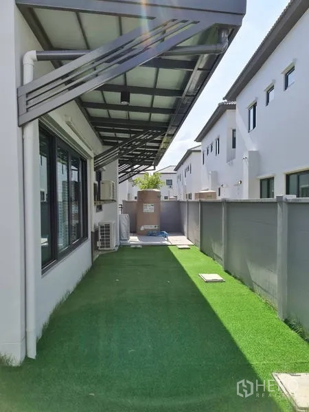 Detached House for rent in Samut Prakan - Covered side yard with metal awning and green turf walkway beside the house.