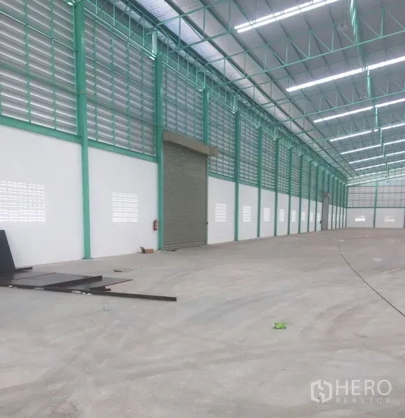 货栈 出租在Samut Prakan - 仓库长跨通道，设百叶通风与宽幅卷闸门，金属屋面下的混凝土地面平整。