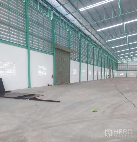 货栈 出租在Samut Prakan - 仓库长跨通道，设百叶通风与宽幅卷闸门，金属屋面下的混凝土地面平整。