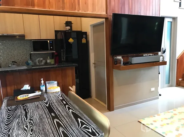 Townhouse for sale in Suan Luang, Bangkok - Open-plan dining and TV corner with wall‑mounted screen and warm wood accents