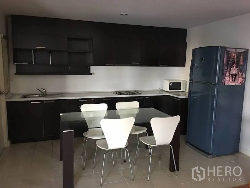 公寓 出租或出售在Yan Nawa, Bangkok - 现代厨房，深色橱柜，玻璃餐桌与四把白色餐椅，大型蓝色冰箱。