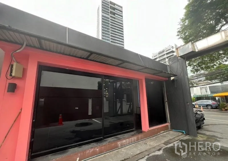 พื้นที่ขายปลีก ให้เช่าในWatthana, Bangkok - ด้านหน้าร้านชั้นเดียว กรอบสีชมพู กระจกสีดำ มีตึกสูงด้านหลัง