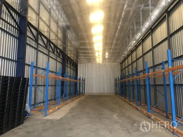 货栈 出租在Pak Kret, Nonthaburi - 暖武里Pak Kret高挑仓库通道，蓝色钢制货架与隔热金属屋顶。