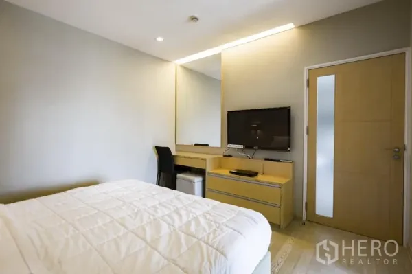 Condominium for rent in Khlong Toei, Bangkok - Cozy bedroom with queen bed, wall-mounted TV, dressing desk and mirror in warm wood tones.