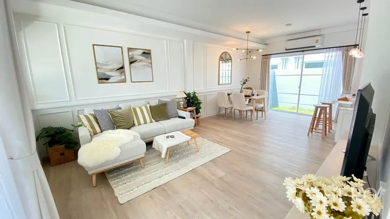Townhouse for rent in Prawet, Bangkok - Spacious lounge with sectional sofa, wall moulding, dining set and full-height windows bringing in natural light.