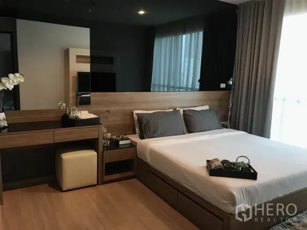 Condominium for rent in Sathon, Bangkok - Cozy master bedroom with wood headboard, vanity desk, large window and full-length curtains.