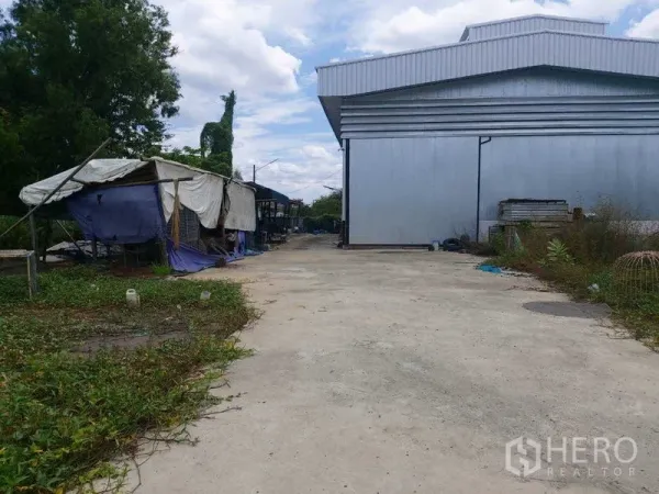 货栈 出售在Mueang Nonthaburi, Nonthaburi - 宽阔混凝土车道与金属外墙仓库，旁有帆布棚与绿地。