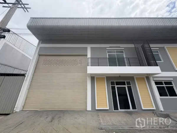 Factory for rent in Phra Samut Chedi, Samut Prakan - Modern factory facade with large roller shutter, balcony and glass doors.