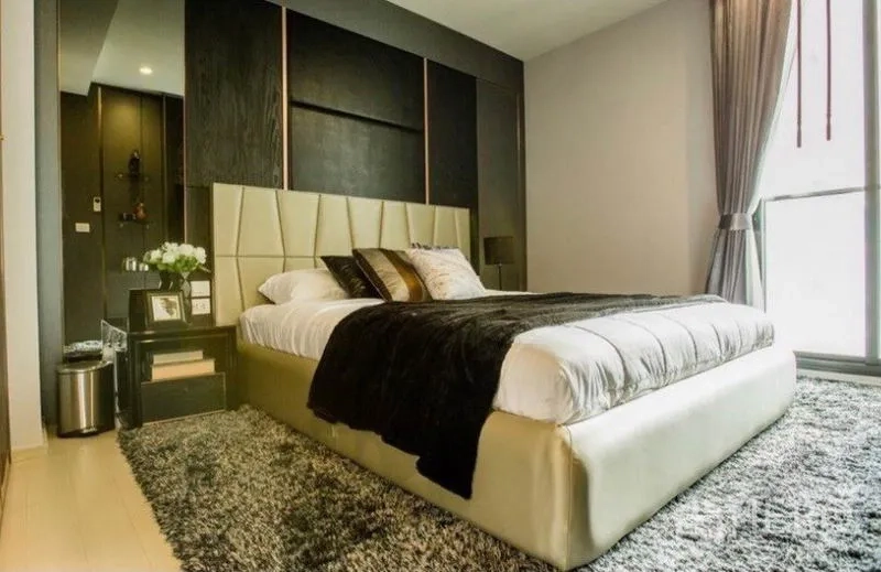 Condominium for rent in Pathum Wan, Bangkok - Second bedroom with upholstered bed, textured wall panel and plush area rug.