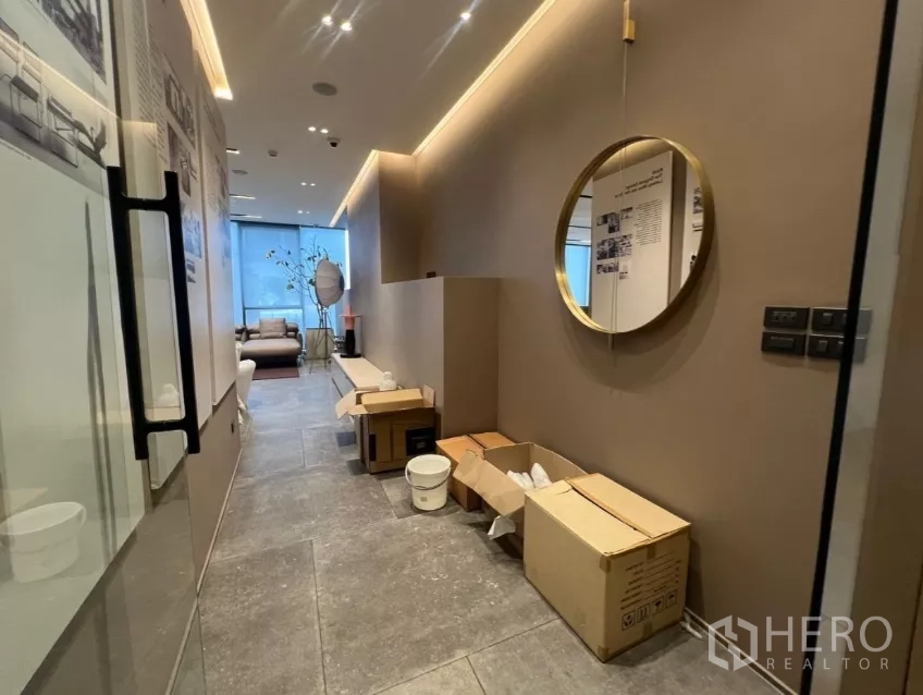 零售空间 出租 - 入口走廊设玻璃门与圆形镜，石材地面上有纸箱通向主空间。