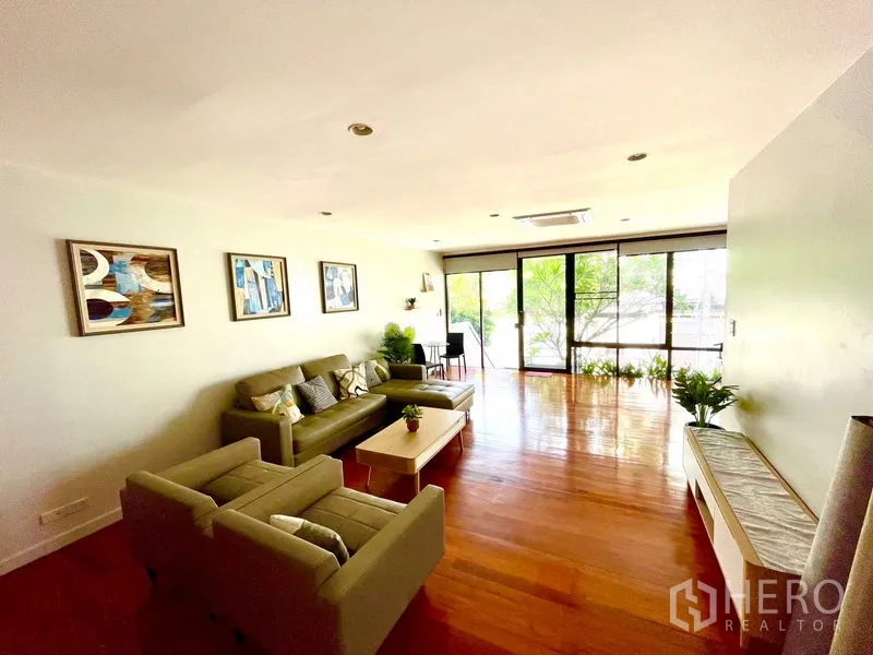 Townhouse for rent in Khlong Toei, Bangkok - Second lounge with grey sofas, wood floors and sliding doors to balcony greenery.