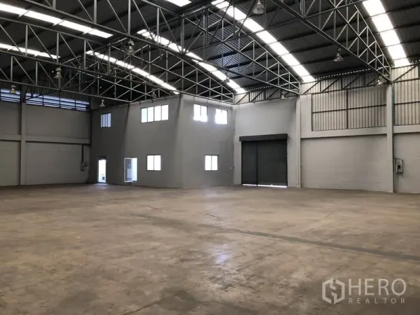 Factory for rent in Pathum Thani - Wide manufacturing space with arched metal roof, corner office and large shutter door.