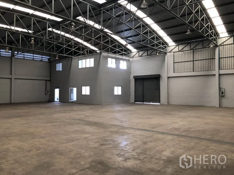 Factory for rent in Pathum Thani - Wide manufacturing space with arched metal roof, corner office and large shutter door.