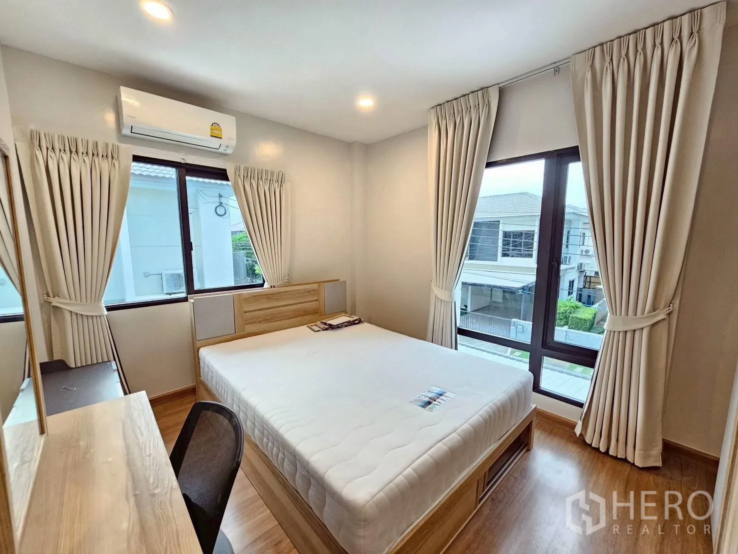 独立式住宅 出售在Bang Phli, Samut Prakan - 转角卧室，Queen床，大窗与浅色窗帘，梳妆书桌与木地板。