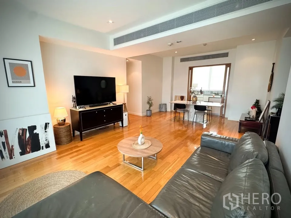 Condominium for rent or sale in Khlong Toei, Bangkok - Living room with large TV console, coffee table, leather sofa, and a sliding door to the kitchen.