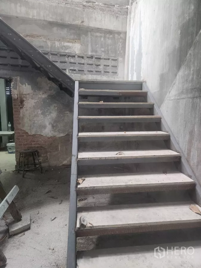 Shophouse for rent in Watthana, Bangkok - Close-up of a sturdy metal staircase in a raw concrete-walled interior.