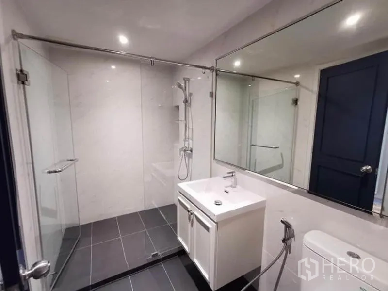 Condominium for rent in Sathon, Bangkok - Modern bathroom with glass shower enclosure, large mirror and white vanity.