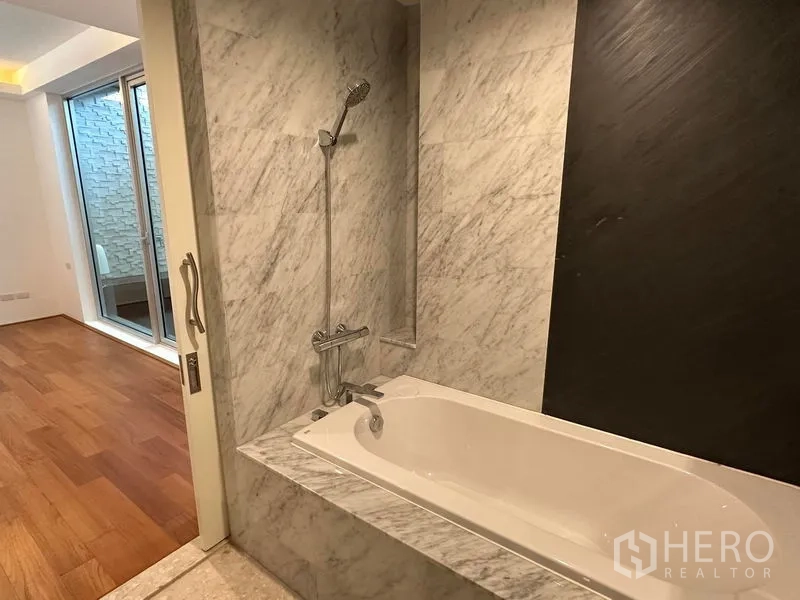 Townhouse for sale in Yan Nawa, Bangkok - Marble bathtub with handheld shower adjoining a bedroom with wood floors and sliding glass doors
