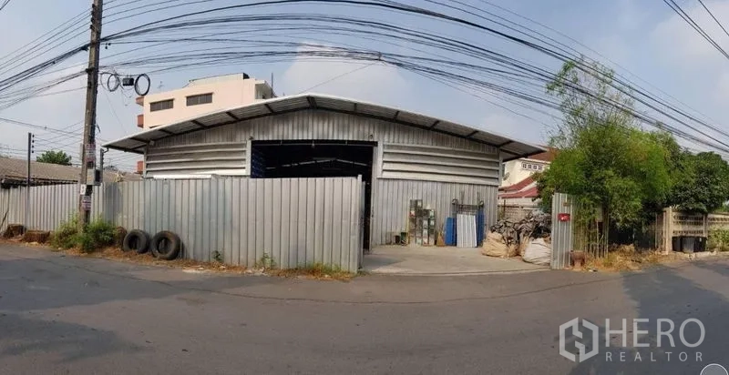 คลังสินค้า ให้เช่าในSai Mai, Bangkok - มุมมองด้านหน้าถนนของโกดังผนังเมทัลชีทในเขตสายไหม กรุงเทพฯ พร้อมประตูรั้วและทางเข้า-ออก.