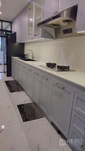Detached House for sale in Sai Mai, Bangkok - Long linear kitchen with white countertops, gas hobs and marble-look floor tiles.