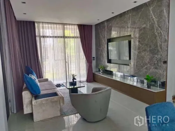 Detached House for rent in Bang Phli, Samut Prakan - Bright living room with marble feature wall, built-in TV console and floor-to-ceiling windows with sheer curtains.
