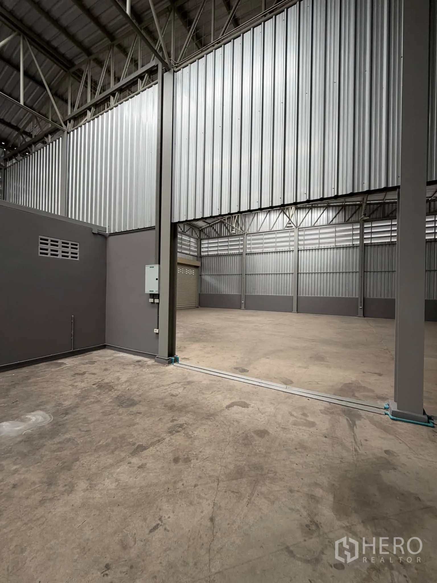 Warehouse for rent in Phra Pradaeng, Samut Prakan - Opening between connected bays with steel cladding, exposed trusses, and concrete floor.