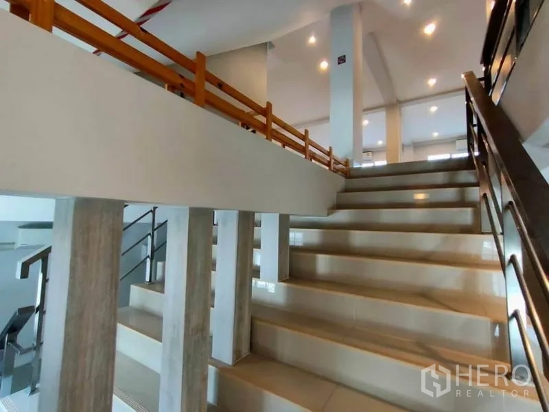 Home Office for rent or sale in Bang Na, Bangkok - Wide internal staircase with metal and wooden handrails under downlights.
