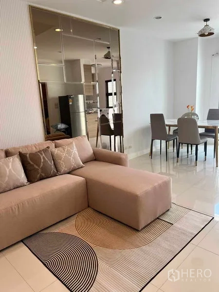 Townhouse for rent in Phra Khanong, Bangkok - Bright open-plan living and dining area with beige sectional sofa, rug and mirrored feature wall.