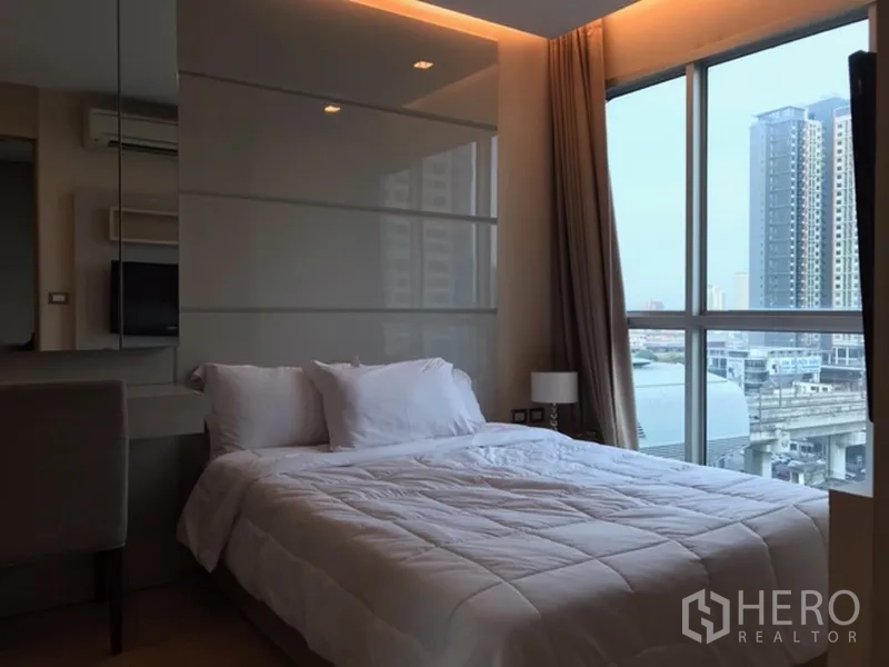 Condominium for rent in Ratchathewi, Bangkok - 1-bedroom with large window and city view, neutral decor and bedside lamp.