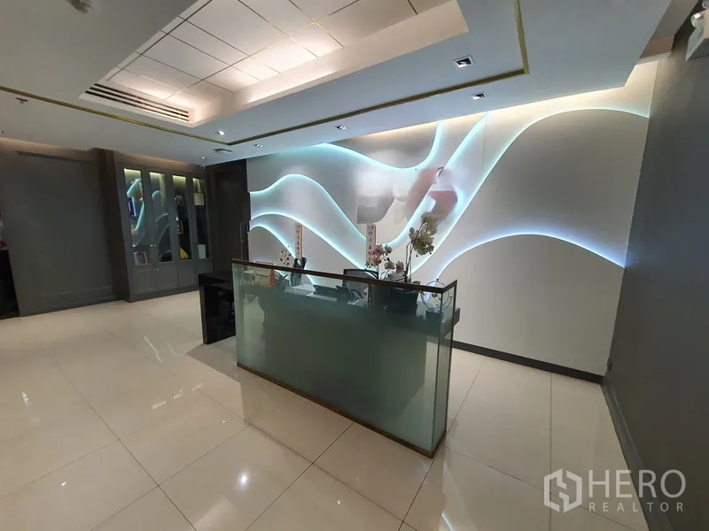 Office Space for rent in Khlong Toei, Bangkok - Contemporary reception with glass desk and wavy backlit feature wall on glossy tiles.