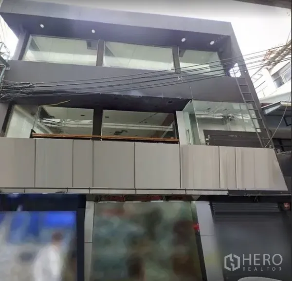 Shophouse for rent in Khlong Toei, Bangkok - Contemporary multi-storey shophouse facade with full-height glass windows above a busy urban street.
