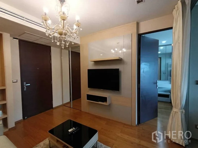 公寓 出租在Ratchathewi, Bangkok - 温馨客厅，水晶吊灯与壁挂电视，通往卧室的门清晰可见。