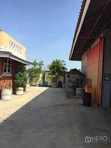 Detached House for rent or sale in Bang Bua Thong, Nonthaburi - Wide side yard between the house and warehouse-style building with greenery.