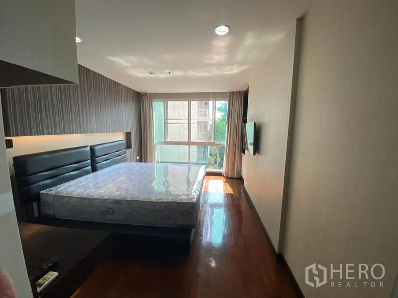 公寓 出租在Watthana, Bangkok - 明亮卧室配大床、木地板与落地窗，视野绿意盎然。