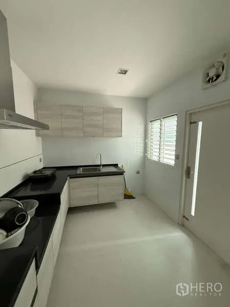 Detached House for rent or sale in Bang Bua Thong, Nonthaburi - Bright Thai kitchen with white cabinetry, black countertops, window and rear door.