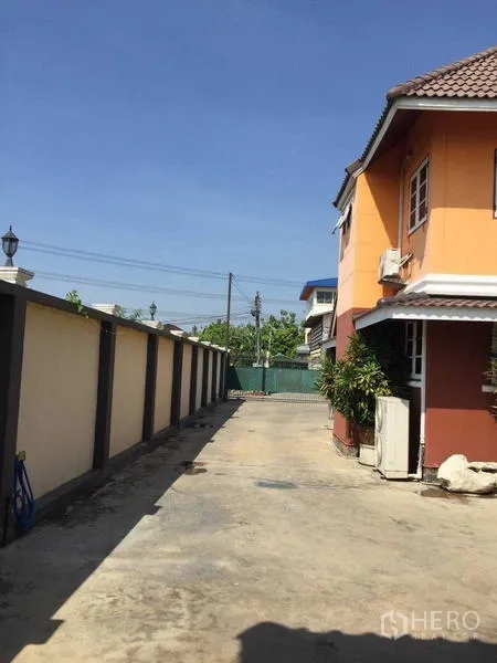 Detached House for rent or sale in Bang Bua Thong, Nonthaburi - Long driveway along a perimeter wall leading to a green gate beside the house.