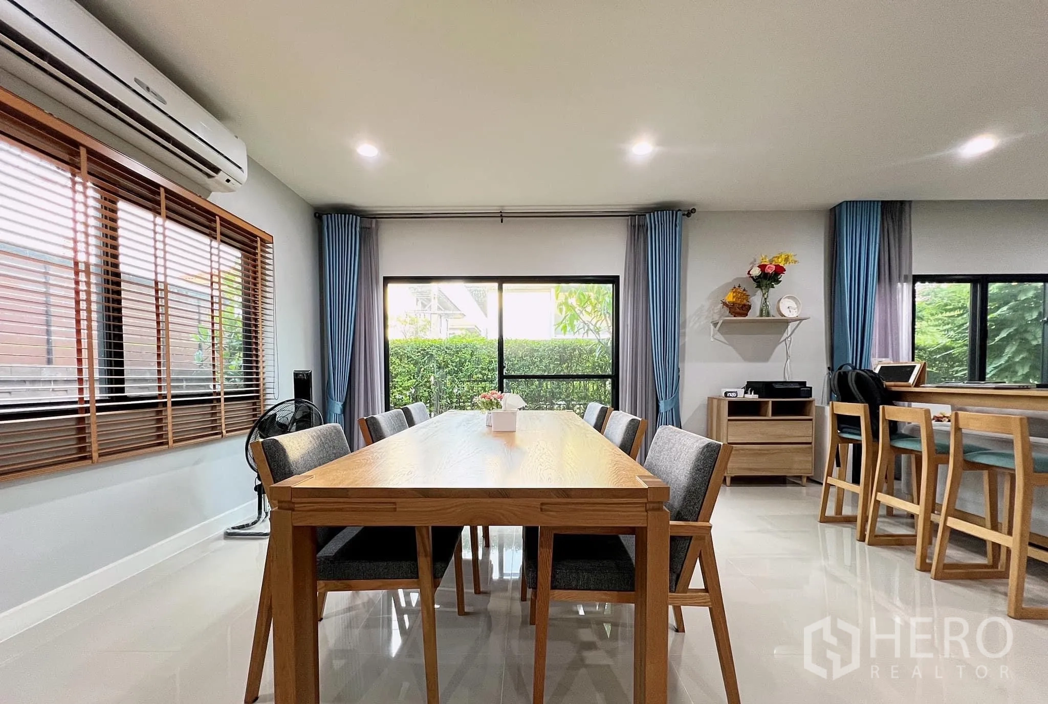Detached House for rent or sale in Lam Luk Ka, Pathum Thani - Eight-seat dining area beside windows with blue curtains and garden outlook.