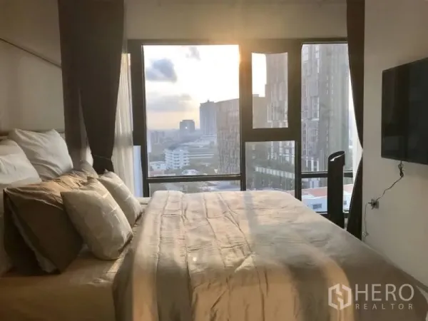 Condominium for rent or sale in Khlong Toei, Bangkok - Bedroom with floor-to-ceiling windows, city view and wall-mounted TV at sunset.