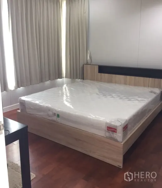 Condominium for rent in Khlong Toei, Bangkok - Bright bedroom with new queen mattress on wood platform bed, light curtains and wood floors.